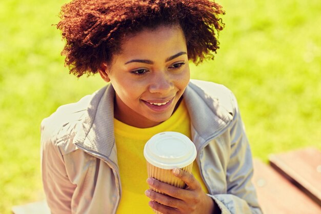 drinks and people concept - smiling african american young woman or teenage girl drinking coffee from paper cup outdoors