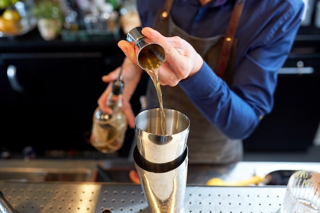 drinks, people and luxury concept - bartender pouring alcohol from jigger into shaker and preparing cocktail at bar