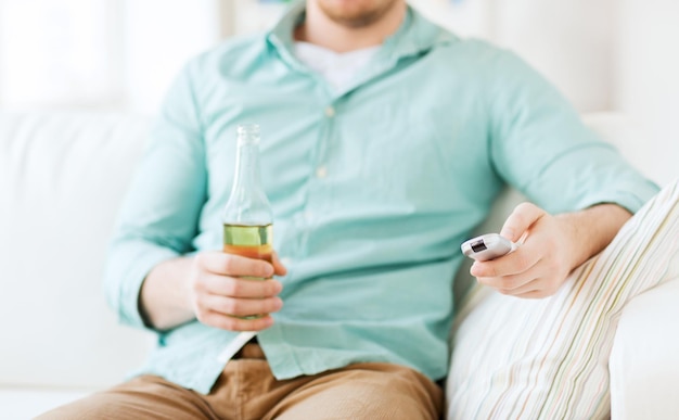 drinks, television, leisure and people concept - man changing tv channels and drinking beer at home