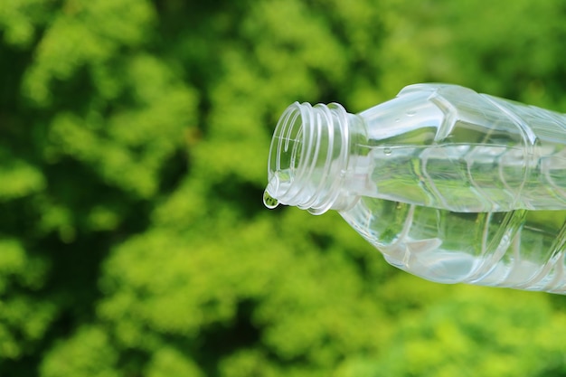 Drinkwater dat uit een PET-fles valt met wazig groen gebladerte op de achtergrond