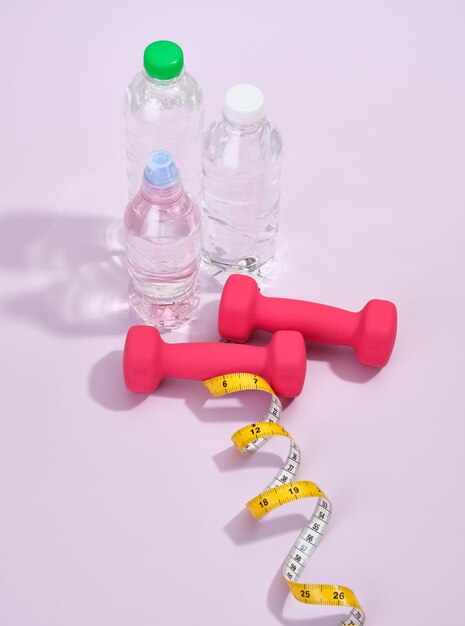 Drinkwater met roze halters en een meetlint op tafel Sportbenodigdheden voor een gezond mooi lichaam