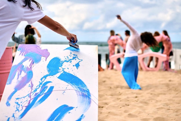 Drip painting outdoor art performance with dancing girls on sandy sea beach Painter artist drawing on white canvas abstract picture in drip painting abstract art technique Creative art festival