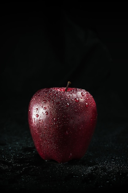 A dripping red apple stands alone on a black background