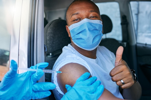 Drive thru covid and corona virus vaccine site as a public\
service for the people man giving thumbs up and endorsing the jab\
while wearing a mask to avoid infection approving being\
vaccinated