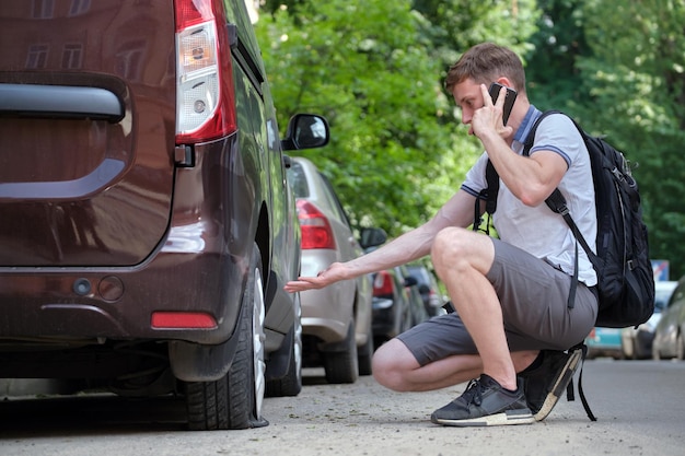 Driver calling road service for assistance having vehicle\
trouble with punctured flat tire on car parked on roadside