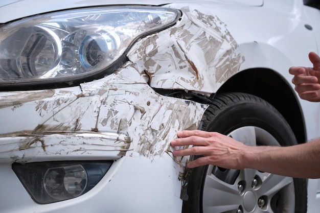 Driver hand examining dented car with damaged fender parked on city street side. Road safety and vehicle insurance concept.