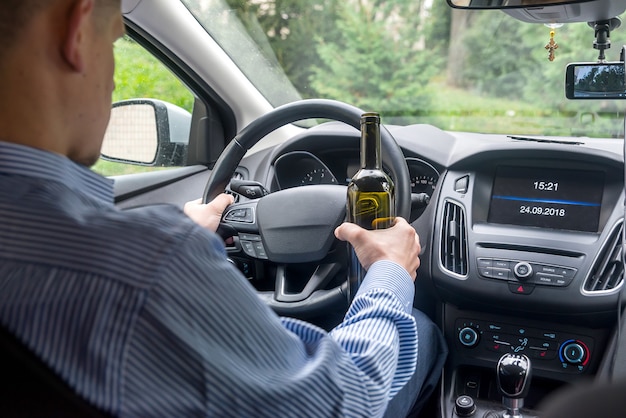 Driver holding steering wheel and bottle of alcohol beverage