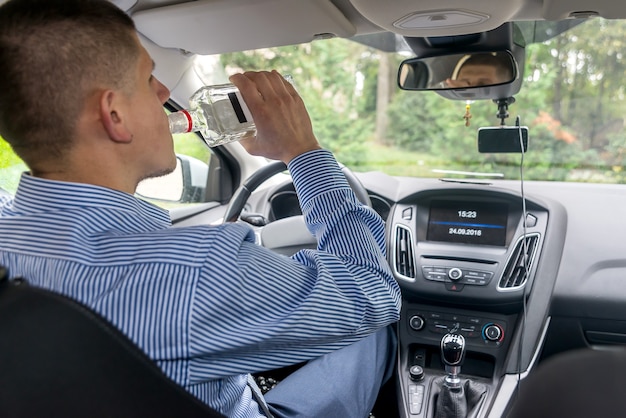 Uomo del conducente che beve alcol durante la guida dell'auto