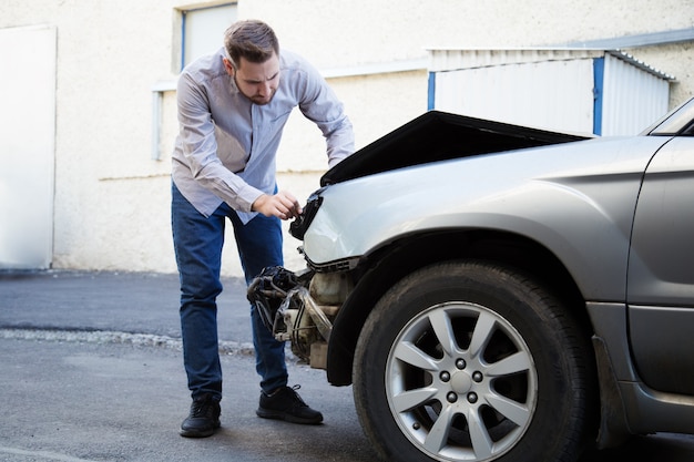 Driver man looking on wrecked car in car accident. man regrets about fixing car headlight after auto crash. tragedy car collision. dangerous road traffic situation.