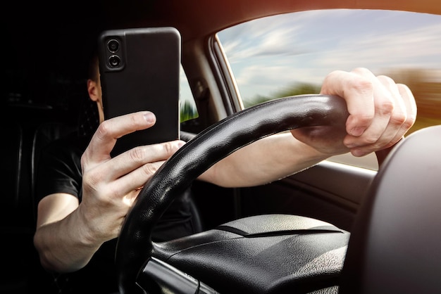 The driver at the wheel of a car uses a smartphone distracted from the road