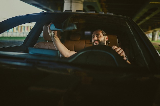 Alla guida di un'auto giovane uomo dai capelli scuri bello alla guida di un'auto