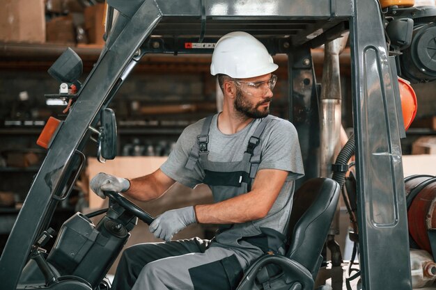 Фото Водитель вилочного погрузчика молодой фабричный работник в серой форме