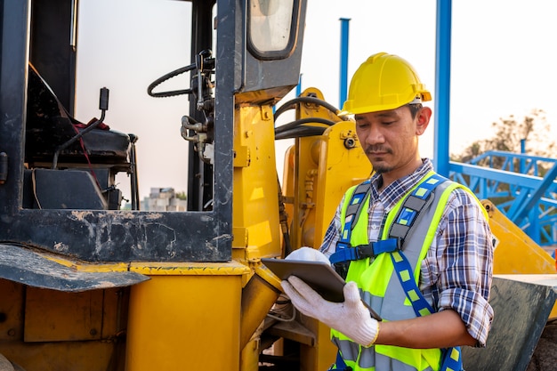 Driving worker heavy wheeled tractor, workers drive orders\
through the tablet, wheel loader excavator with backhoe unloading\
sand works in construction site.