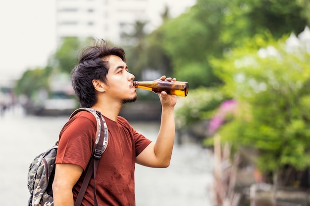 Droevig alleenstaand Aziatisch mens het drinken bier bij openbaar park