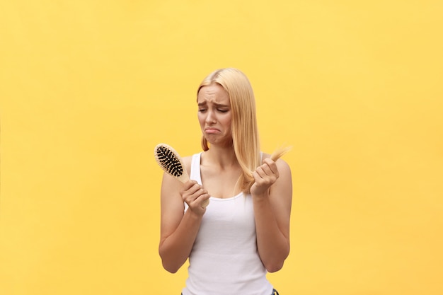 Droevig meisje die haar beschadigd haar met in hand kam bekijken