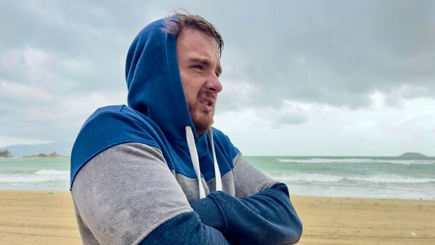 Droevig, overstuur, gefrustreerd, bevroren man op het strand, zee bij koud weer, slechte vakantie.