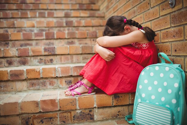 Droevig schoolmeisje met hoofd in haar benen