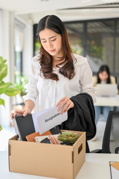 Droevige en ongelukkige jonge Aziatische vrouwelijke kantoormedewerker die haar spullen in een kartonnen doos verpakt