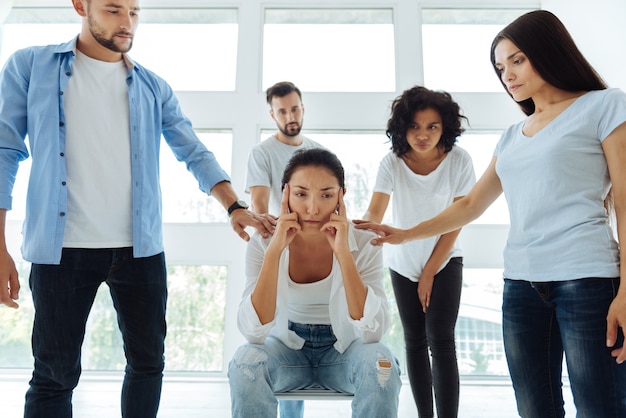 Droevige humeurige jonge vrouw die haar slapen vasthoudt en zich op haar problemen concentreert terwijl ze in het midden van de cirkel zit