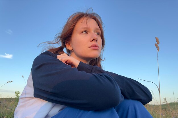 Droevige jonge vrouw die alleen zit in een veldzonsondergang bij zomerweer