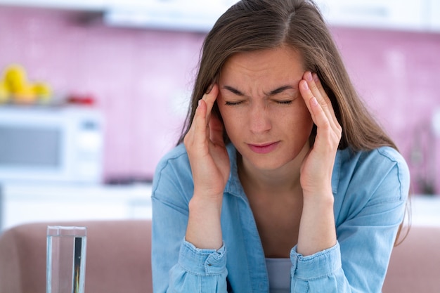 Droevige ongelukkige beklemtoonde jonge vrouw die aan hoofdpijn thuis lijdt. Migraine en lichamelijke vermoeidheid voelen