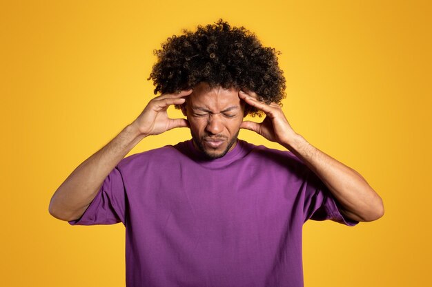 Foto droevige volwassen afro-amerikaanse gekrulde man in paars t-shirt drukt handen naar tempels die lijden aan