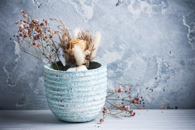 Droge bloemen in blauwe pot op witte houten tafel.