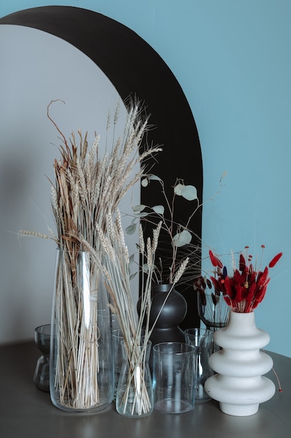 Foto droge bloemen in vazen op een houten tafel tegen de blauwe muur met boog herfst decoratieve compositie verticaal