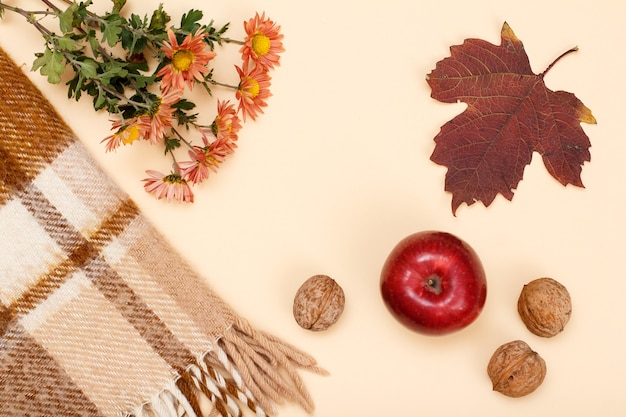 Droge gele en bruine bladeren, boeket bloemen, rode appel, walnoten en geruite plaid op de beige achtergrond. Een herfstcompositie. Bovenaanzicht.