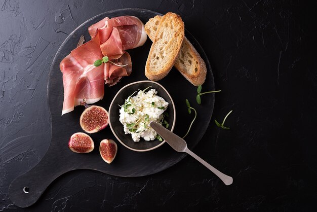 Droge gerookte ham met sneetjes brood op een zwarte achtergrond, Italiaanse voorgerecht prosciutto met fruit en kaas, close-up.