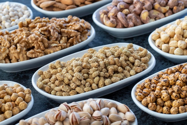 Droge moerbei in selectieve aandacht Noten op plaat op een donkere achtergrond Walnoot Kikkererwten Witte kikkererwten Droge moerbei amandel cashew pistache Soorten noten op de plaat