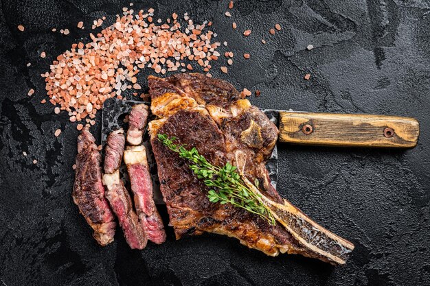 Droge oude gegrilde Tomahawk of cowboy beef steak op een vleesmes Zwarte achtergrond Bovenaanzicht