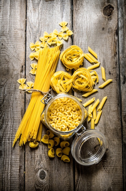 Droge pasta in blikjes en meng de pasta met spaghetti. Op houten achtergrond. Bovenaanzicht