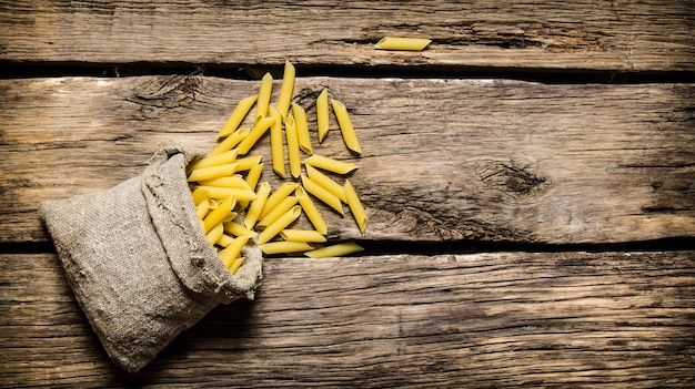 Droge pasta in de oude zak. Op de houten tafel. Vrije ruimte voor tekst. Bovenaanzicht