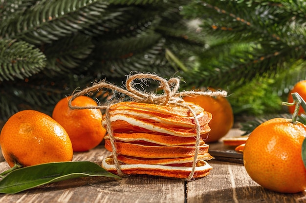 Droge sinaasappelschijfjes snack. gedroogde citrusvruchten voor kerstversiering. mandarijnen met bladeren, dennentakken, schaar en draad. houten achtergrond, rustiek concept, close-up