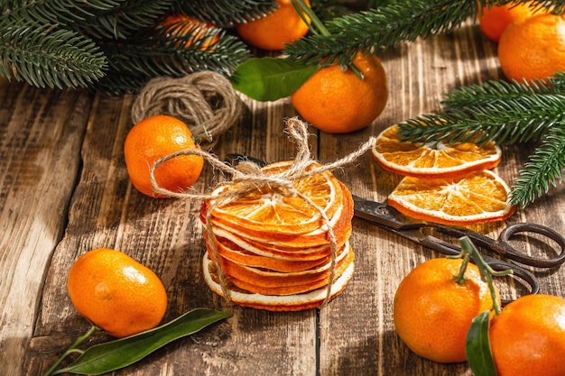 Droge sinaasappelschijfjes snack. gedroogde citrusvruchten voor kerstversiering. mandarijnen met bladeren, dennentakken, schaar en draad. houten achtergrond, rustiek concept, kopieer ruimte