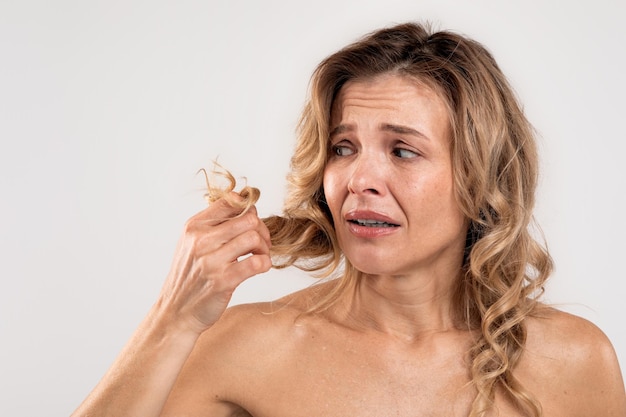 Droge uiteinden Gestresste vrouw van middelbare leeftijd die naar haar beschadigde haar kijkt