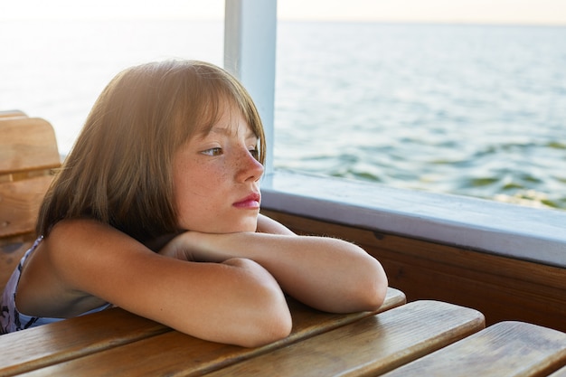 Dromerig klein vrouwelijk kind dat op houten lijst leunt terwijl het hebben van reis op boot