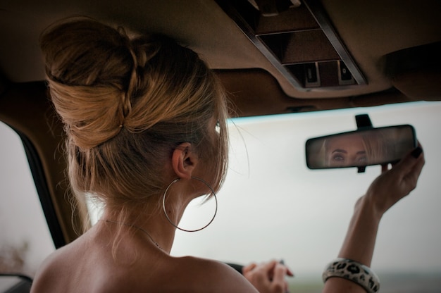Dromerige blonde vrouw die in de spiegel in de auto kijkt