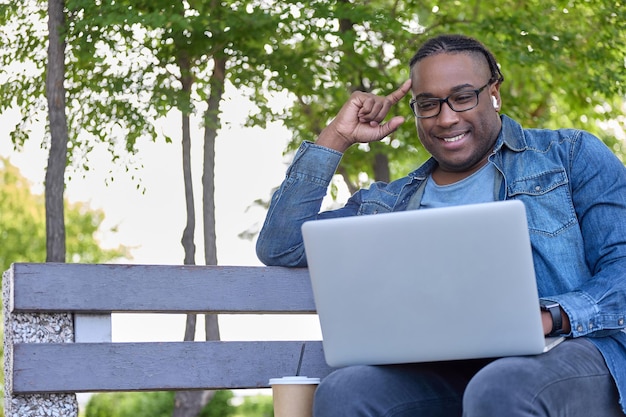 Dromerige zwarte schrijver zit op een bankje in het park zijn verhaal op te schrijven