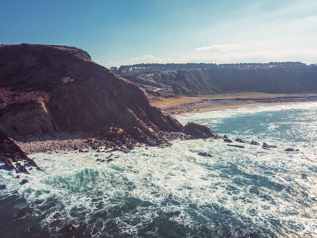 Drone aerial view of the cliffs with lots of waves on a rocky and sandy beach