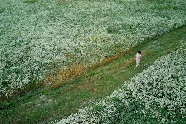 花が咲く牧草地を歩いてドレスを着た女性のドローン空撮