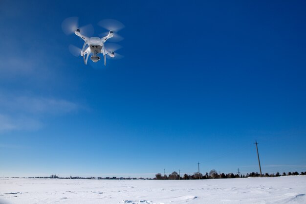 Drone che vola sopra il campo coperto di neve nella soleggiata giornata invernale