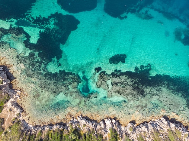 Drone-opname van prachtig kristalhelder turkoois en blauw zeewater, rond een rots en golven die het zandstrand bereiken.