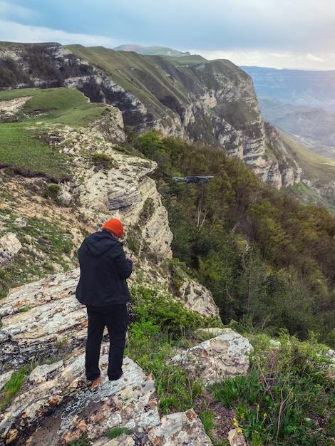 Drone photographer starting a dron in sunrise on a cliff in the mountains. Vertical view.