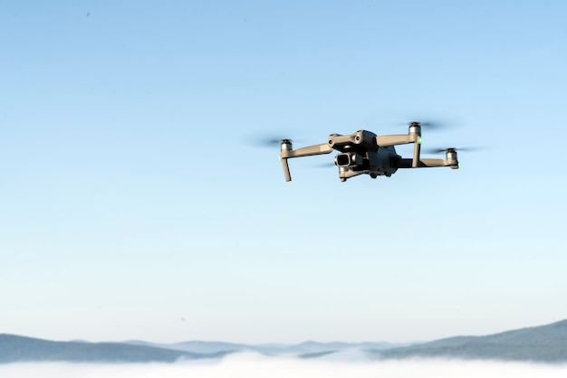 drone quadcopter helicopter in the air, in a clear blue sky, morning fog and mountains below. aerial photo and video shooting using gadgets and modern devices.