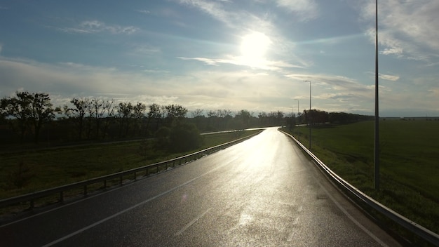 Drone rises above wet asphalt road for cars between sown fields