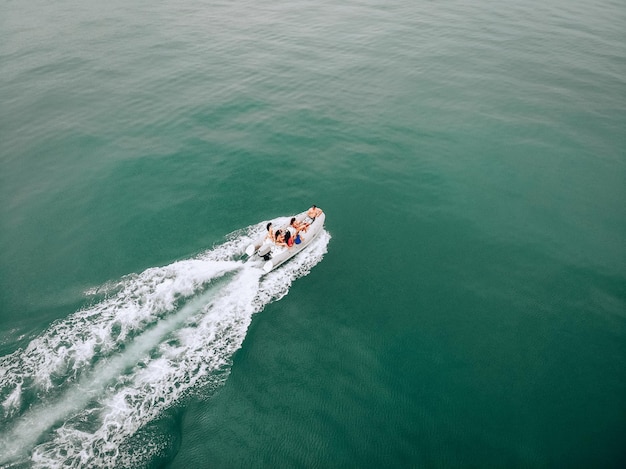 Drone\'s image in open space at sea. young people sail on a\
white motor boat on a hot summer day. beautiful young womens in\
swimsuits communicate with a guy in a black cap and a camera in his\
hands.