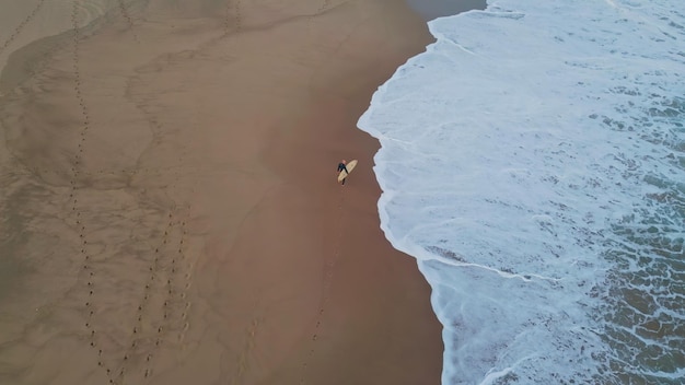 Drone shot unknown surfer walking in sandy beach waiting waves hobby concept