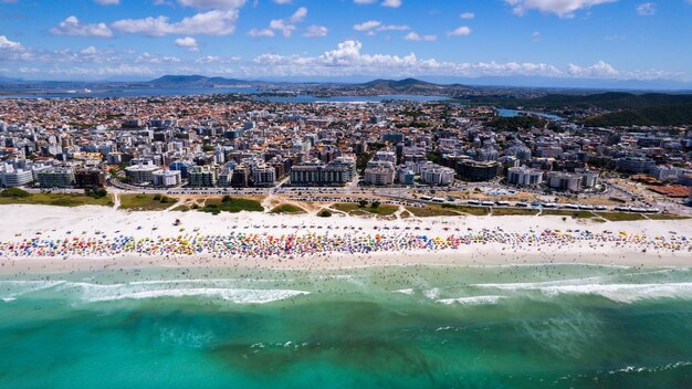 Foto drone-uitzicht op het strand met groene en blauwe zee wit zand met parasols in de stad cabo frio